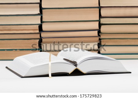 The opened book with a bookmark and the pen against piles of old books