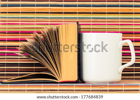 White cup and the opened book nearby on a color background from bamboo sticks