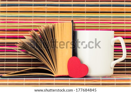 The white cup, the opened book and red heart before them on a color background from bamboo sticks
