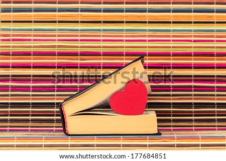 Red heart between pages of the slightly opened book on a color background from bamboo sticks