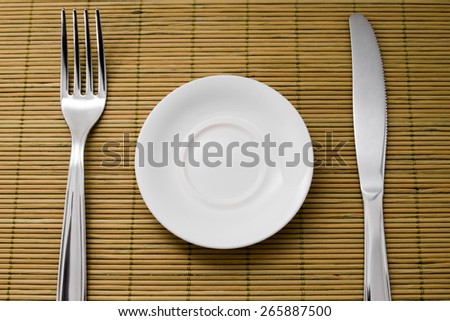 A small plate for diet next to a knife and fork on green bamboo placemats