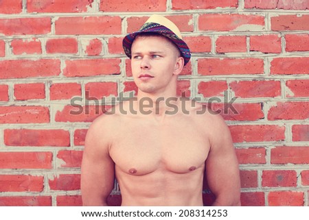 Bodybuilder in a hat stands against the wall and looks into the distance