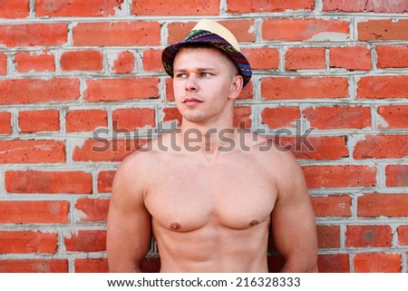 Bodybuilder in a hat stands against the wall and looks into the distance
