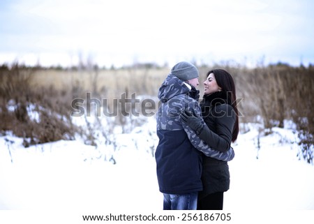 Happy young couple hugging outdoors in a snowy park. Love hugs, family relationships.