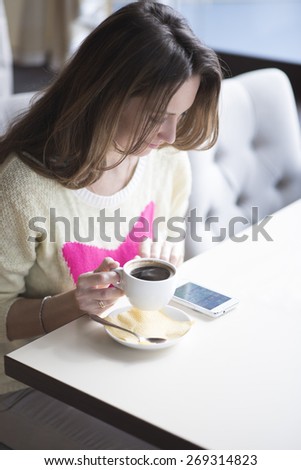 Fashionable girl in yellow blouse sitting in a cafe and drink coffee while viewing the message on the phone.