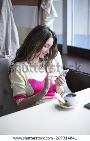 Fashionable girl in yellow blouse sitting in a cafe with coffee and reading messages on social networks.