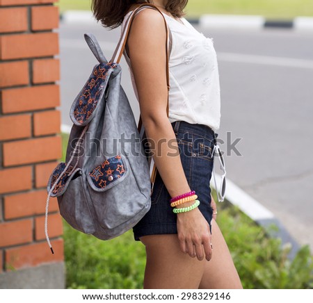 Close up torso of young brunette woman in sexy denim shorts and white T-shirt, with a bag over arm of standing at a brick wall in the city travel, vacation tanned beautiful figure
