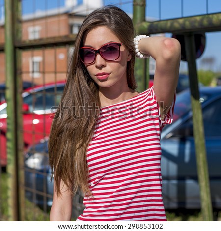 She straightens the hair on the background of the fence, with glasses and a sexy hair, a red shirt, urban life style, enjoying outdoor recreation, a thoughtful look