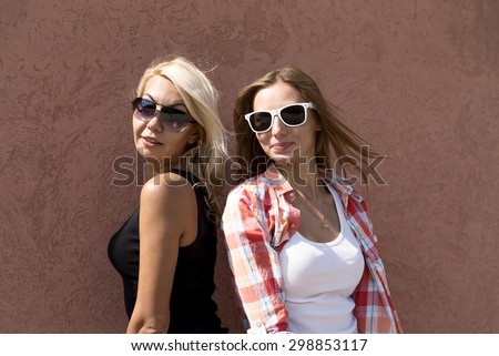 Two beautiful girls on the street smile to rest against the wall, fashion style urban life teen, brunette and blonde in glasses resting enjoy your vacation, happy girlfriend