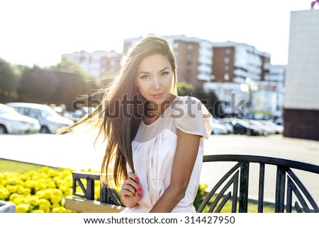 Beautiful girl sitting on a bench, sunny summer day, fashion style urban life, resting in a gentle dress looks sensual, enjoying the summer Woman