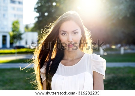 Portrait of a beautiful brunette in a park in bright sunlight. Fashion style of urban life, emotionally looks. Outdoor summer.