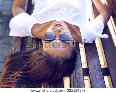 Beautiful brunette student girl lying on a park bench relaxing in the fresh air. Fashion style glamorous woman, summer day in the city during the day on a bench sleeping, sunbathing.