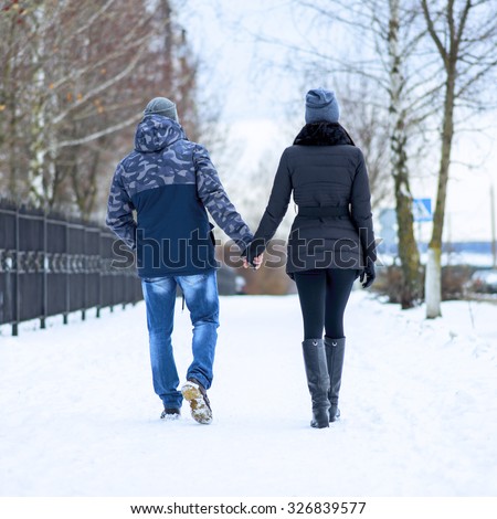 Couple holding each other\'s hands, the winter goes on the road, enjoying a stroll, a love couple. Husband and wife are going through the park holding hands in the winter. The movement of people.