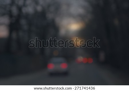 Blurred image of dark gloomy forest road, sunset in stormy sky and car lights