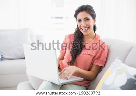 Smiling brunette sitting on her sofa using laptop at home in the sitting room