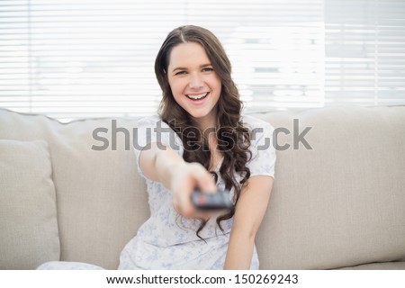 Smiling young woman changing tv station sitting on a cosy couch