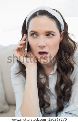 Pretty casual woman being surprised on the phone while sitting on a cosy couch