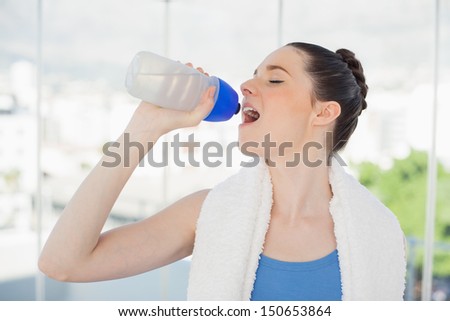 Gorgeous slender woman hydrating after exercising in bright sports hall