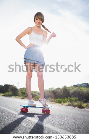 Happy young woman balancing on her skateboard on a deserted road