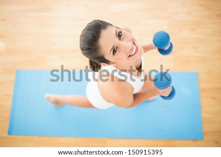 Happy woman exercising with dumbbells on blue exercise mat at home on wooden floor