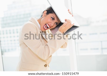 Crazed businesswoman hitting head off laptop in her office