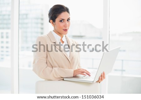 Smiling businesswoman standing behind her chair holding laptop in her office
