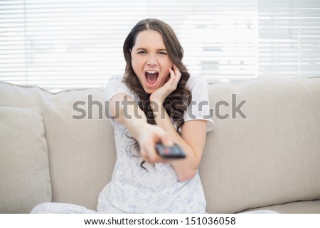 Scared young woman changing tv station sitting on a cosy couch