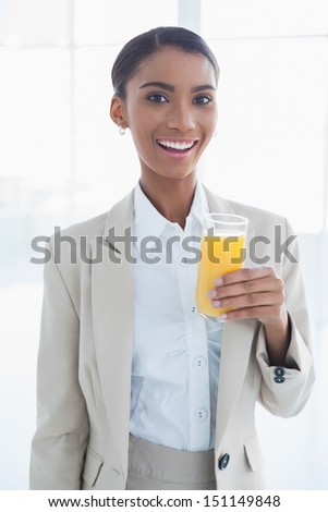 Smiling elegant businesswoman in bright office holding glass of orange juice