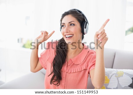 Dancing brunette sitting on her sofa listening to music at home in the sitting room