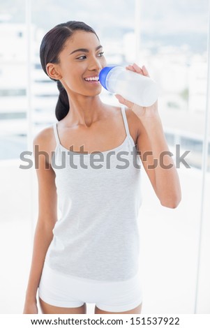 Cheerful sporty model drinking water from her flask in bright room at home