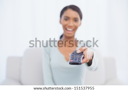 Cheerful woman sitting on sofa in bright living room changing tv channel