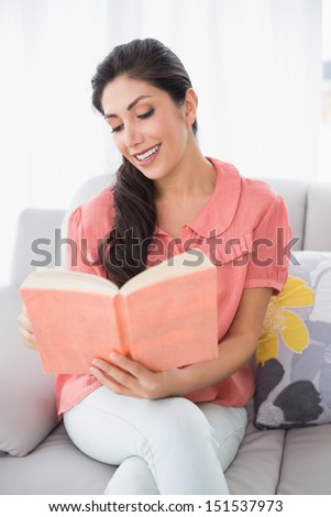 Content brunette sitting on her sofa reading a book at home in the sitting room