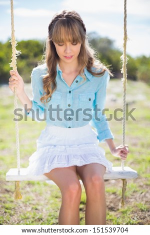 Pensive young model posing in a sunny garden while sitting on swing