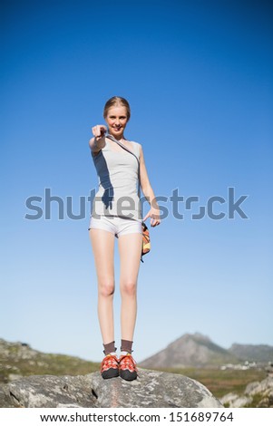 Smiling woman standing on rock pointing at camera