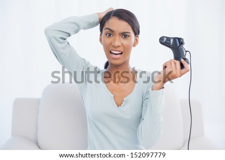 Irritated pretty woman sitting on sofa in bright living room playing video games