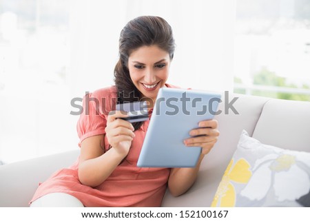 Happy brunette sitting on her sofa using tablet to shop online at home in the sitting room