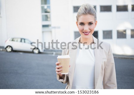 Cheerful stylish businesswoman holding coffee outside on urban background
