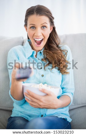 Surprised woman sitting on sofa in bright living room changing tv channel