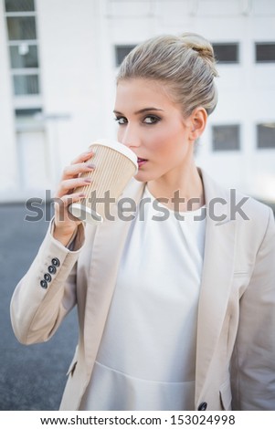 Gorgeous stylish businesswoman drinking coffee outside on urban background