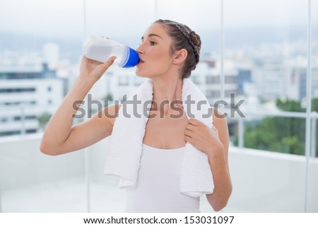 Cute sporty brunette hydrating after exercising in bright fitness studio