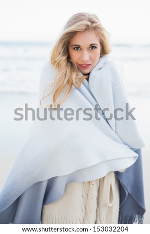 Fashion blonde woman covering herself in a blanket on the beach