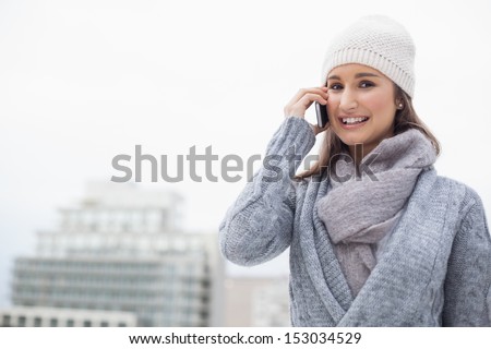 Content brunette with winter clothes on having a call outdoors on a cold grey day