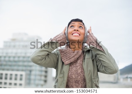 Troubled young model in winter clothes clogging her ears outside on a cloudy day