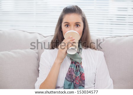 Smiling pretty model drinking coffee sitting on cozy sofa