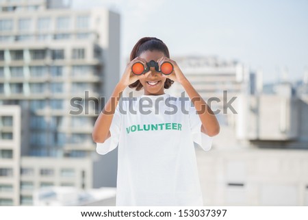Smiling woman with volunteer tshirt using binoculars outdoors on urban background