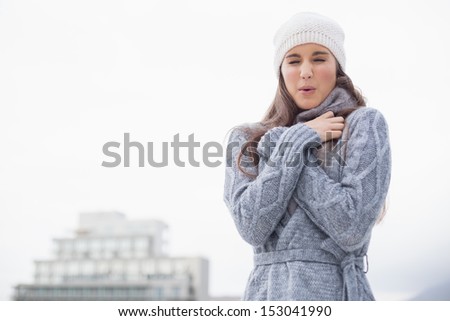 Shivering pretty woman with winter clothes on posing outdoors on a cold grey day