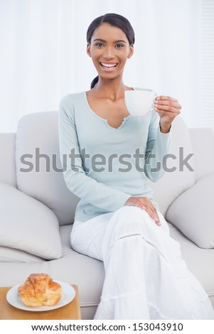 Smiling attractive woman holding cup of coffee sitting on cozy sofa