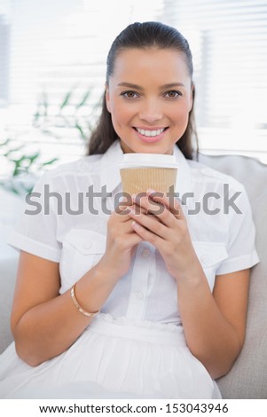 Smiling pretty woman having coffee sitting on cozy couch in bright living room