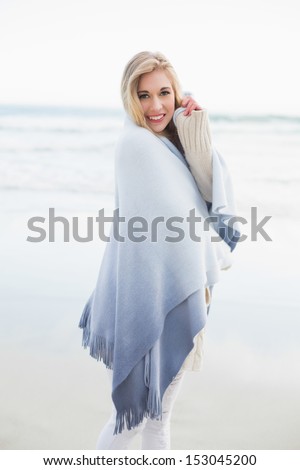 Charming blonde woman covering herself in a blanket on the beach
