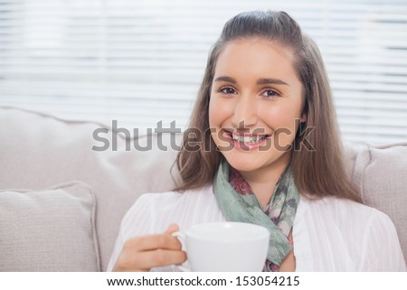Cheerful pretty model holding coffee sitting on cozy sofa